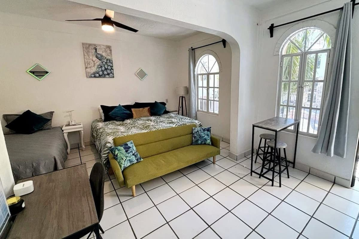 A bedroom with a bed, a desk, a chair, a window with curtains, and a ceiling fan.