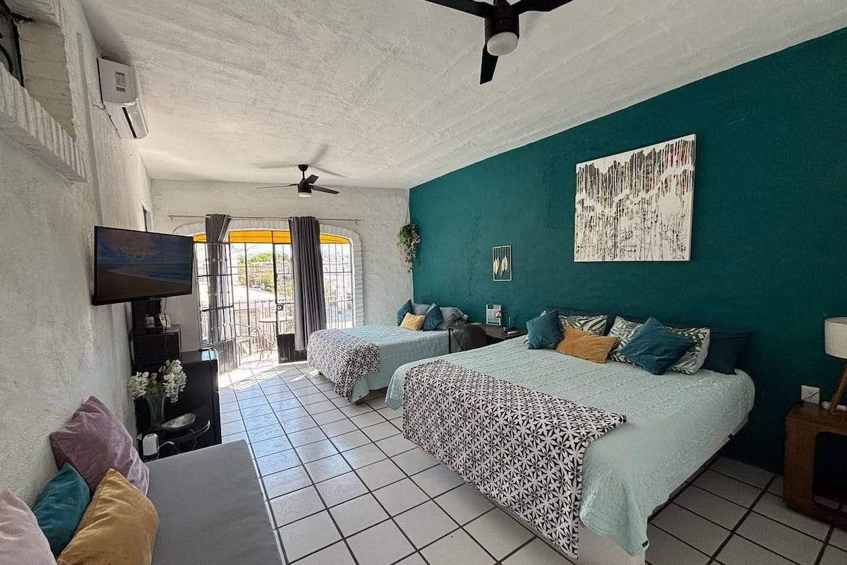 A bedroom with two beds, a TV, and a balcony with a view.
