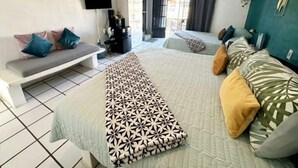 Un dormitorio con una cama, un banco, un televisor y una ventana con cortinas.