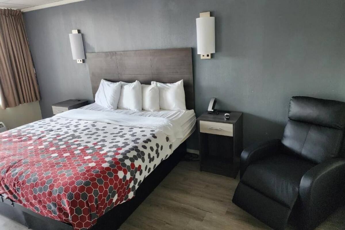 A modern hotel room with a large bed, a black leather chair, and two bedside tables.