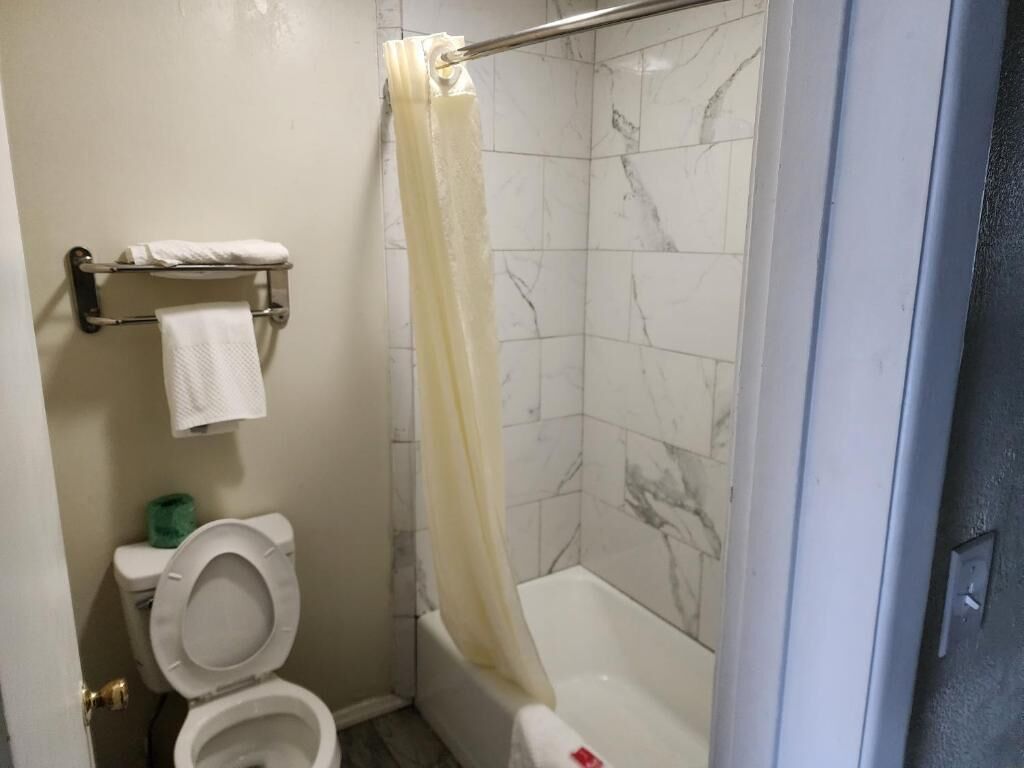 Un baño con inodoro, ducha con cortina y toallero con toallas.