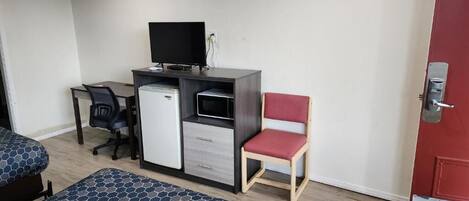 Una habitación de hotel con cama, escritorio, computadora, televisor y una silla roja.
