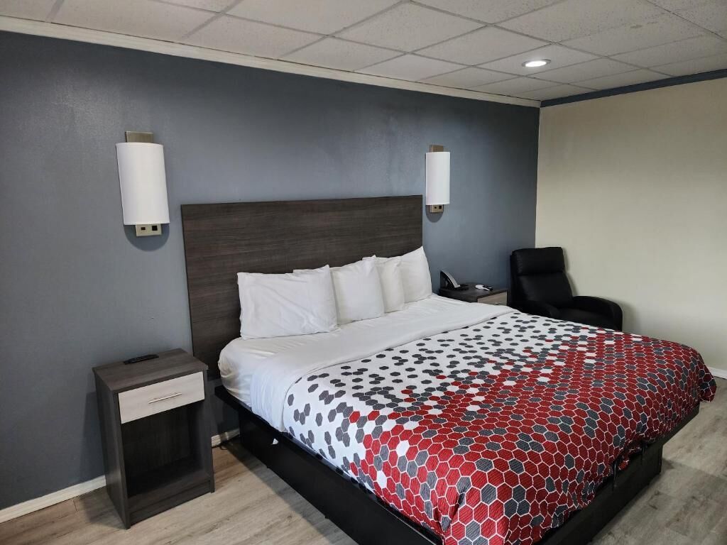 A hotel room with a bed, nightstands, a chair, and wall-mounted lights.