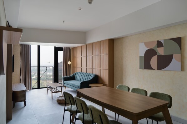 A modern living room with a sofa, dining table, and chairs. There is a large window with a view of the city. - Cove Carstensz BSD (Gading Serpong)