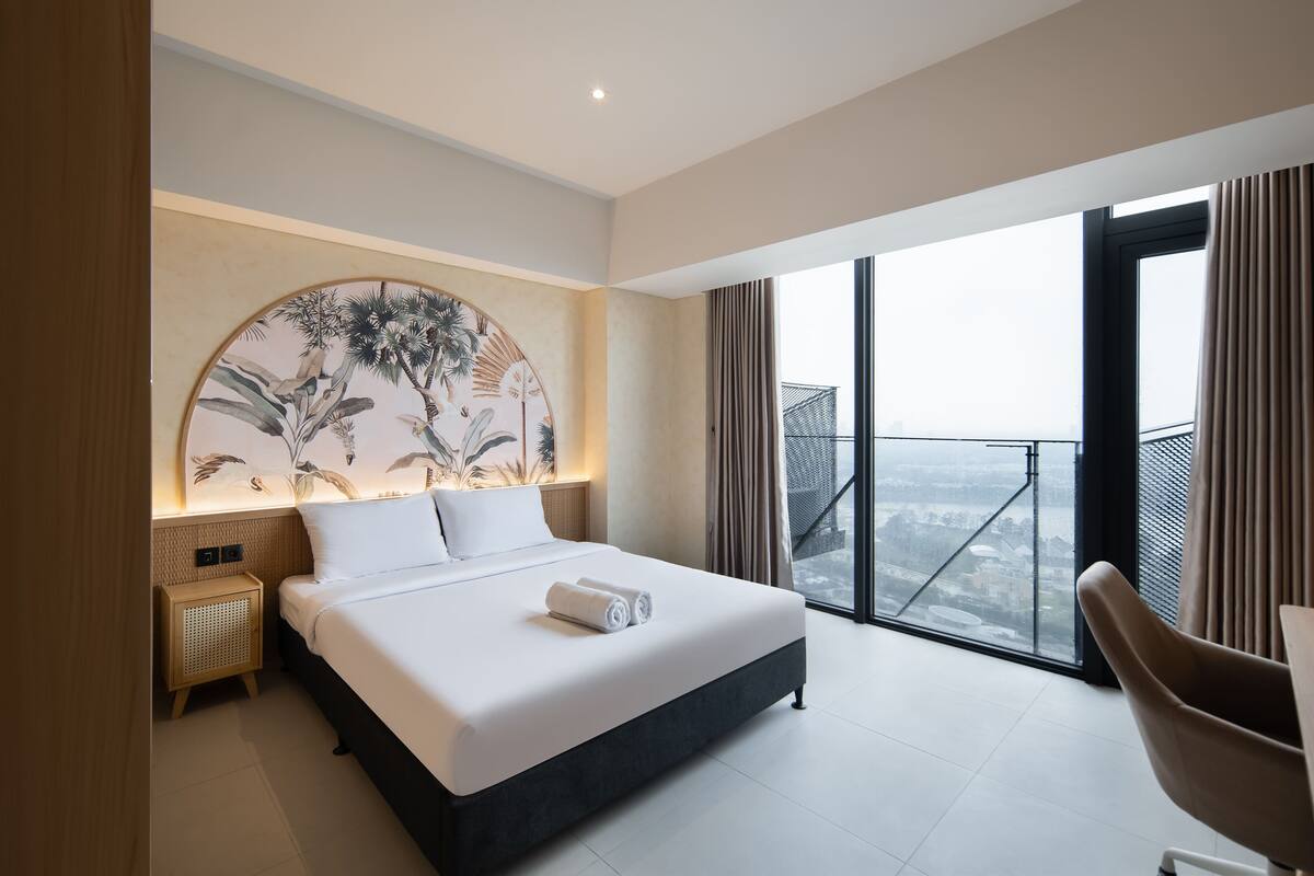 A modern hotel room with a large bed, a view of the city, and a balcony with a railing.