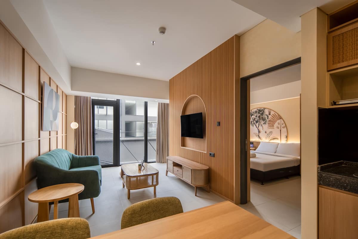 A modern hotel room with a dining area, a sofa, a small table, and a TV mounted on the wall.