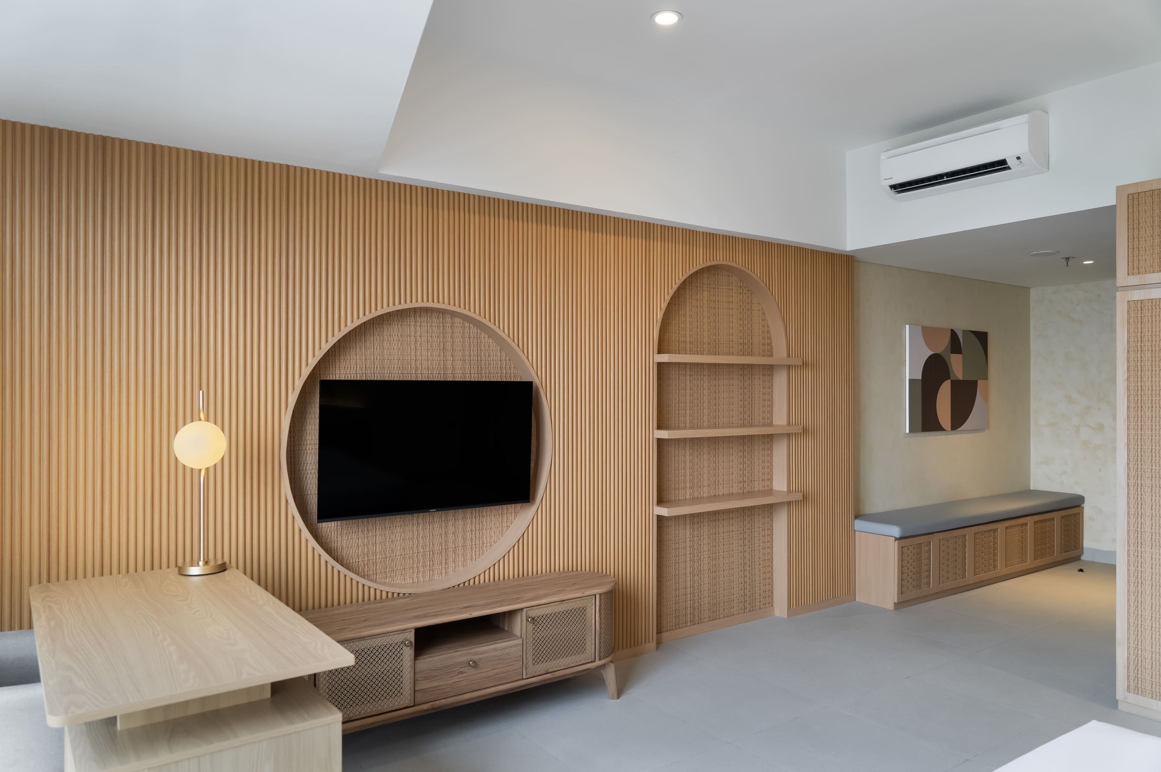 A modern living room with a flat-screen TV, wooden panel walls, a round entertainment unit, and a built-in bench.