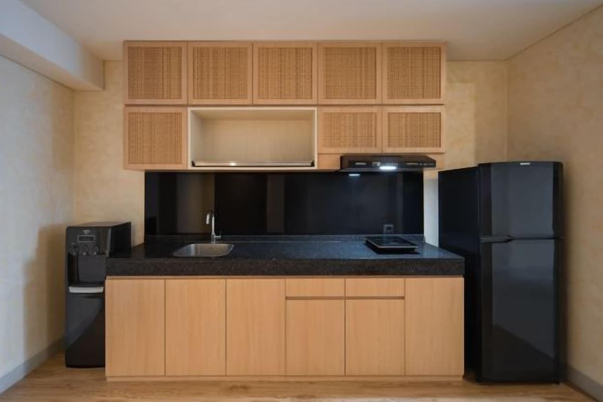 A compact kitchen with wooden cabinets, a black countertop, a built-in oven, and a black refrigerator.