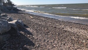 Uma praia rochosa com ondas, céu claro e um edifício com cerca à esquerda.