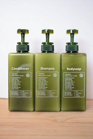Drie flessen huidverzorgingsproducten: conditioner, shampoo en douchezeep, elk met een groene verstuiver en etiketten die het producttype en de specificaties beschrijven.