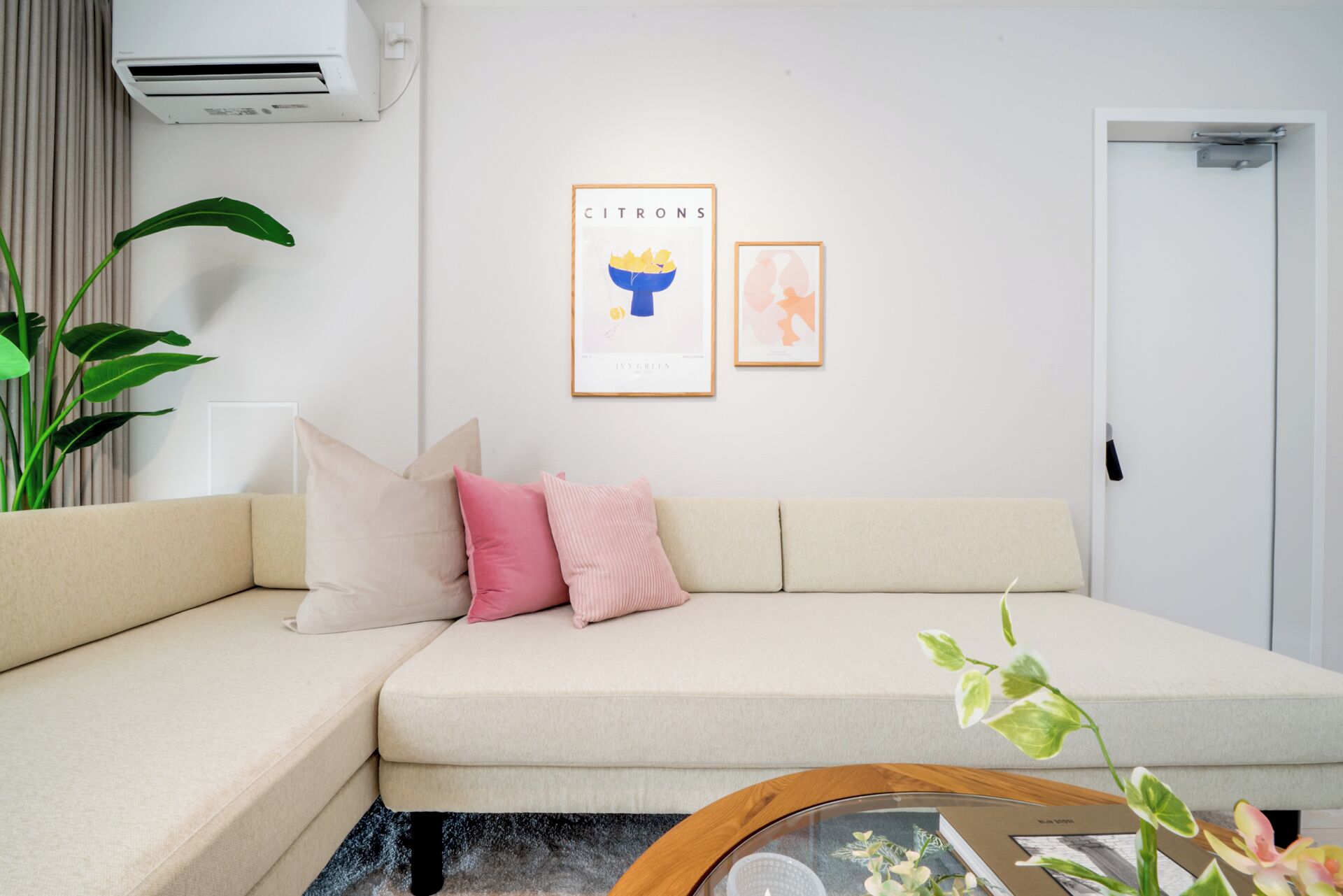 A modern living room with a beige sofa, a coffee table, and a large green plant.