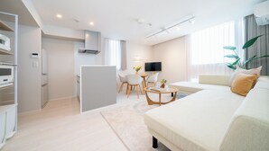 Une chambre d’hôtel moderne dotée d’un canapé, d’un coin repas avec des chaises, d’une télévision et d’un coin cuisine équipé d’appareils électroménagers.