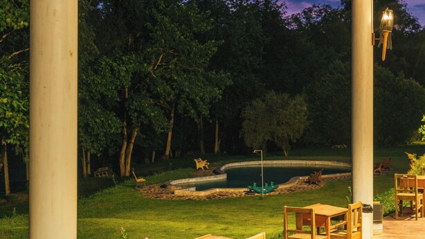 An outdoor seating area with tables and chairs, a pond, and trees in the background.