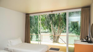 A hotel room with a bed, a desk, and a large window offering a view of trees and a body of water.