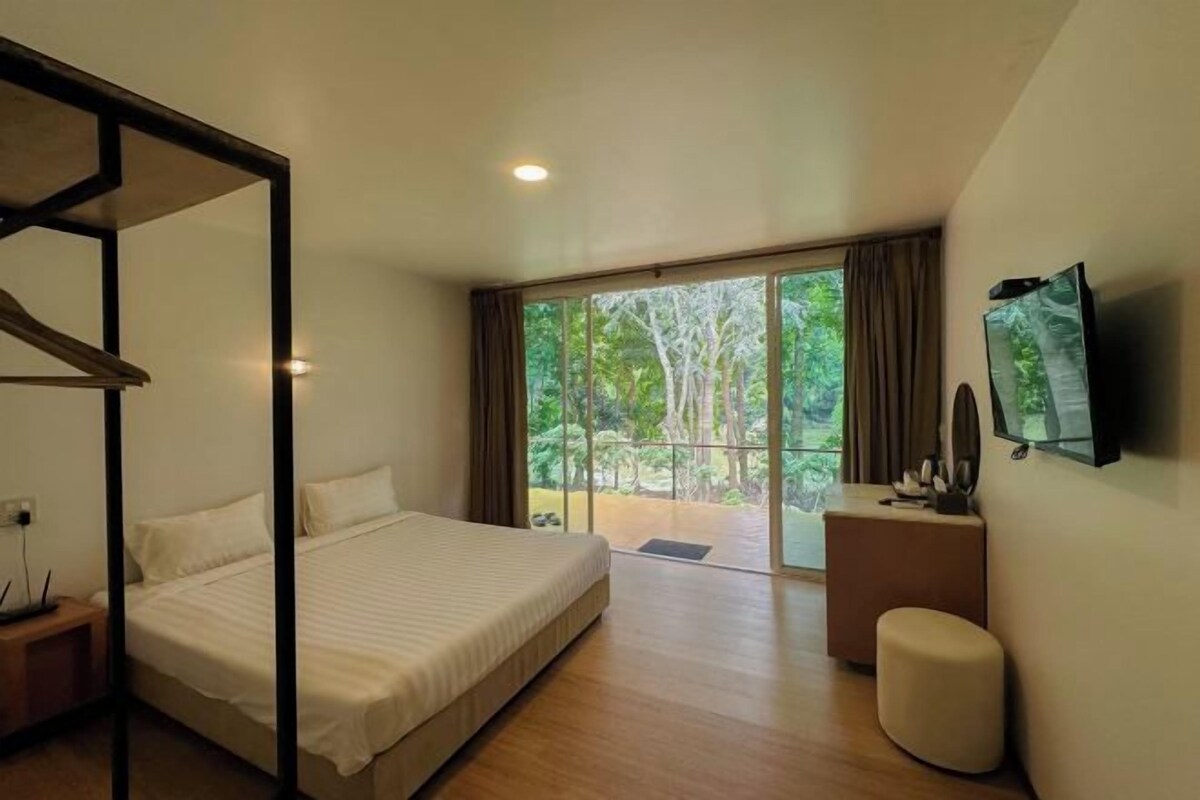 Un dormitorio con una cama grande, televisión y balcón con vistas a árboles.