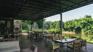 An outdoor dining area with tables and chairs, a covered roof, and a view of a river and forest.