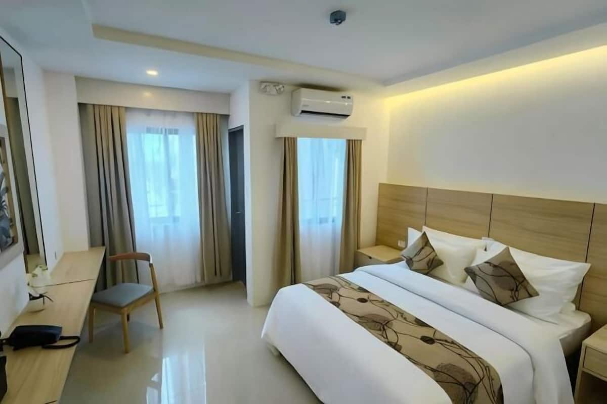 Una habitación de hotel con cama, escritorio, silla, aire acondicionado y cortinas.