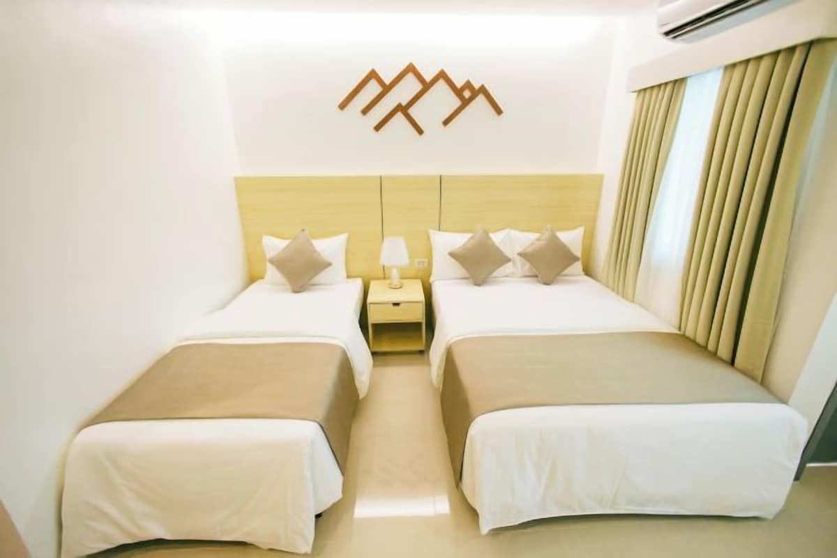 Een hotelkamer met twee bedden, een nachtkastje, een wandairconditioner en een gordijn.