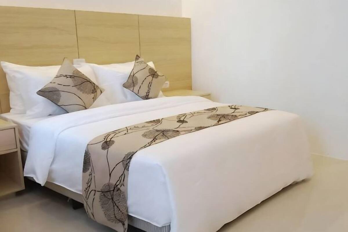 Una cama bien hecha con ropa de cama blanca y almohadones decorativos, un cabecero de madera y una mesita de noche.