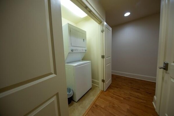 A laundry room with a washing machine and dryer, wooden flooring, and a door leading to another room.