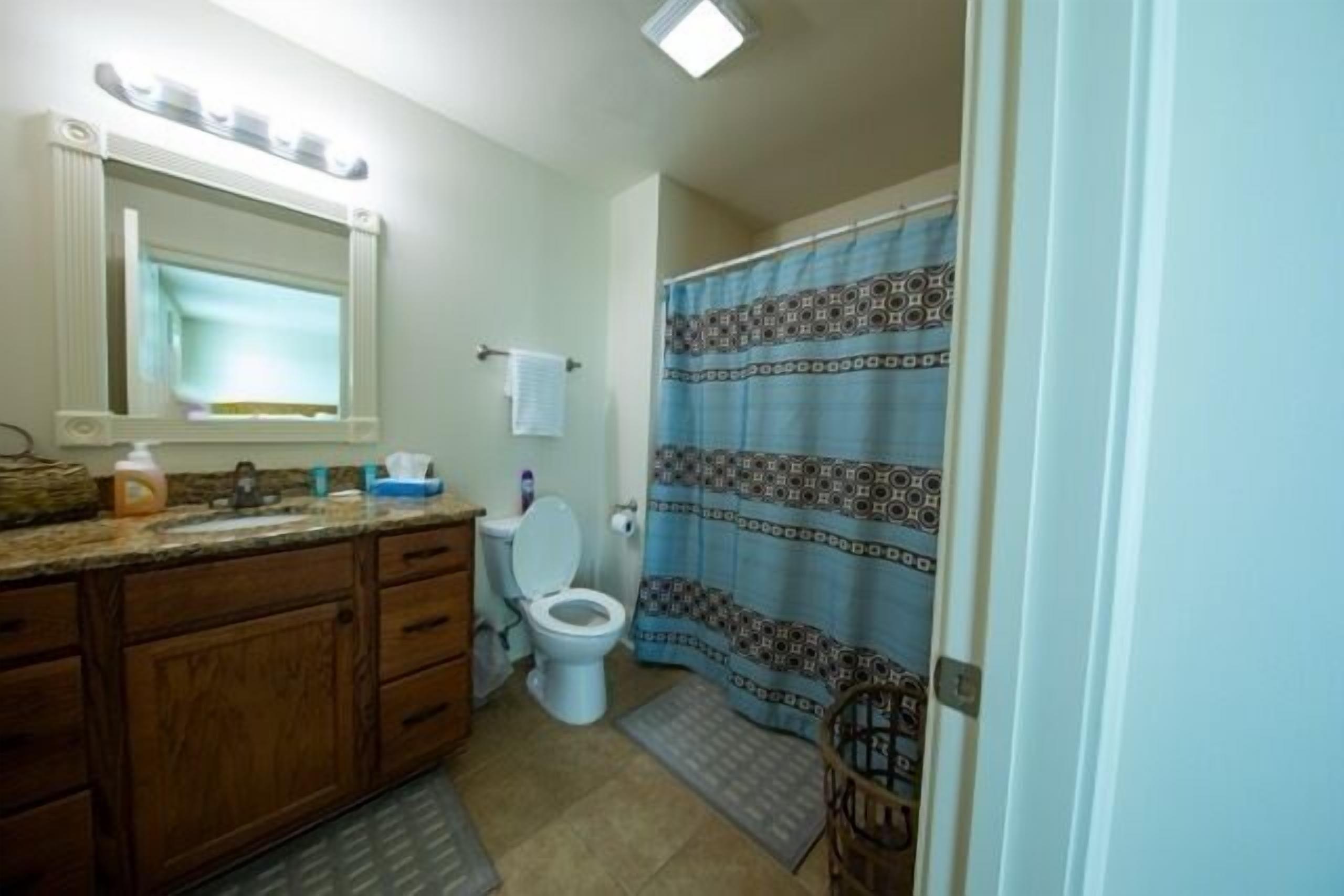 Un baño con tocador de madera, inodoro blanco y cortina de ducha estampada.