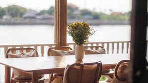 A wooden dining table with chairs, a vase with flowers, and a view of a body of water. - Private Villa (Tambon Ko Kret)