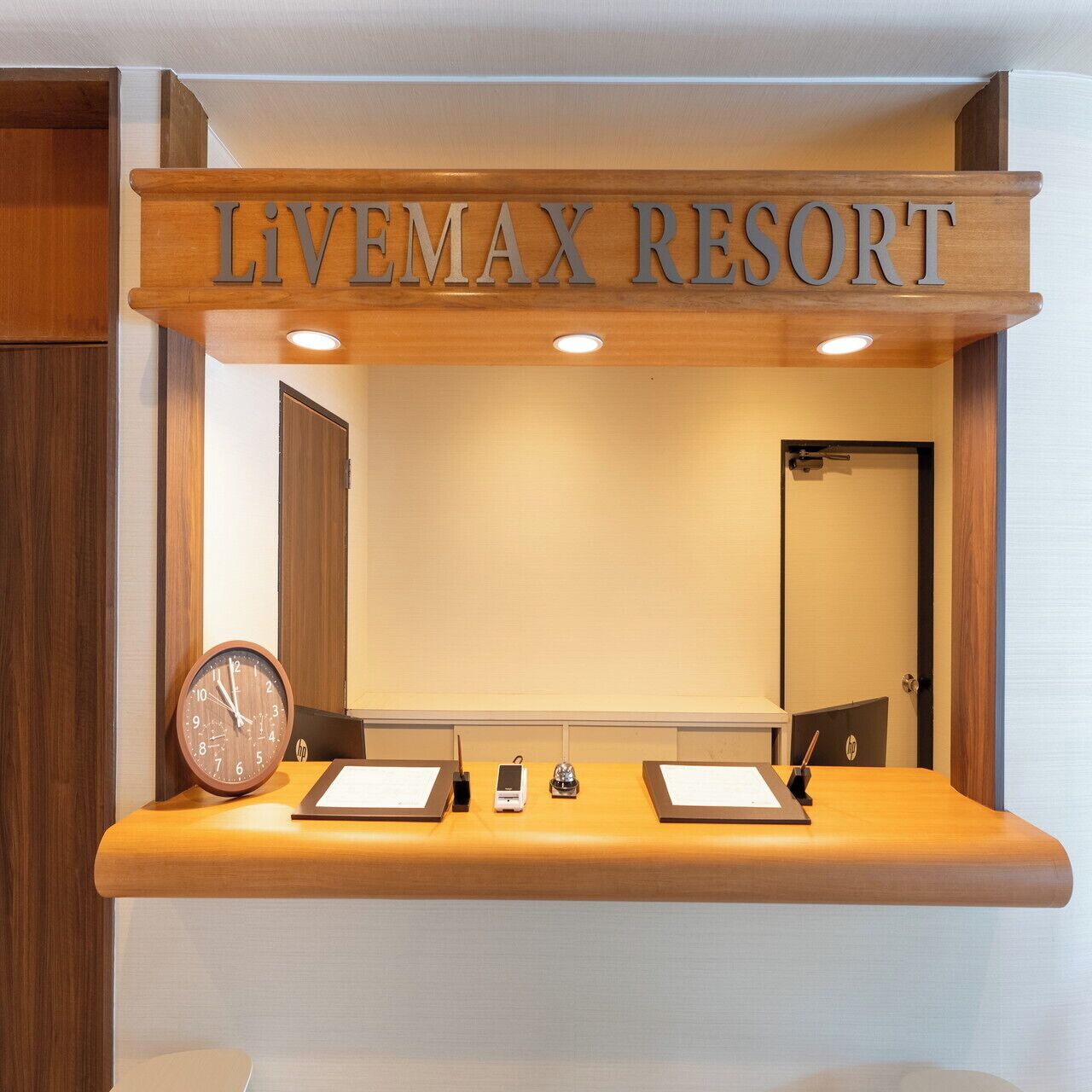 Eine Rezeption im Livemax Resort mit einem Holunderschild, einer Uhr und zwei Informationsblättern auf der Theke.