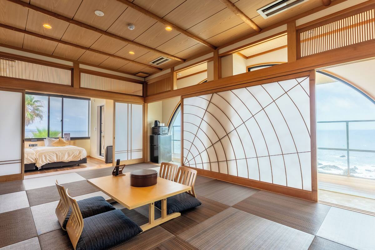Una camera moderna con un letto, un'area da pranzo e ampie finestre vista mare.