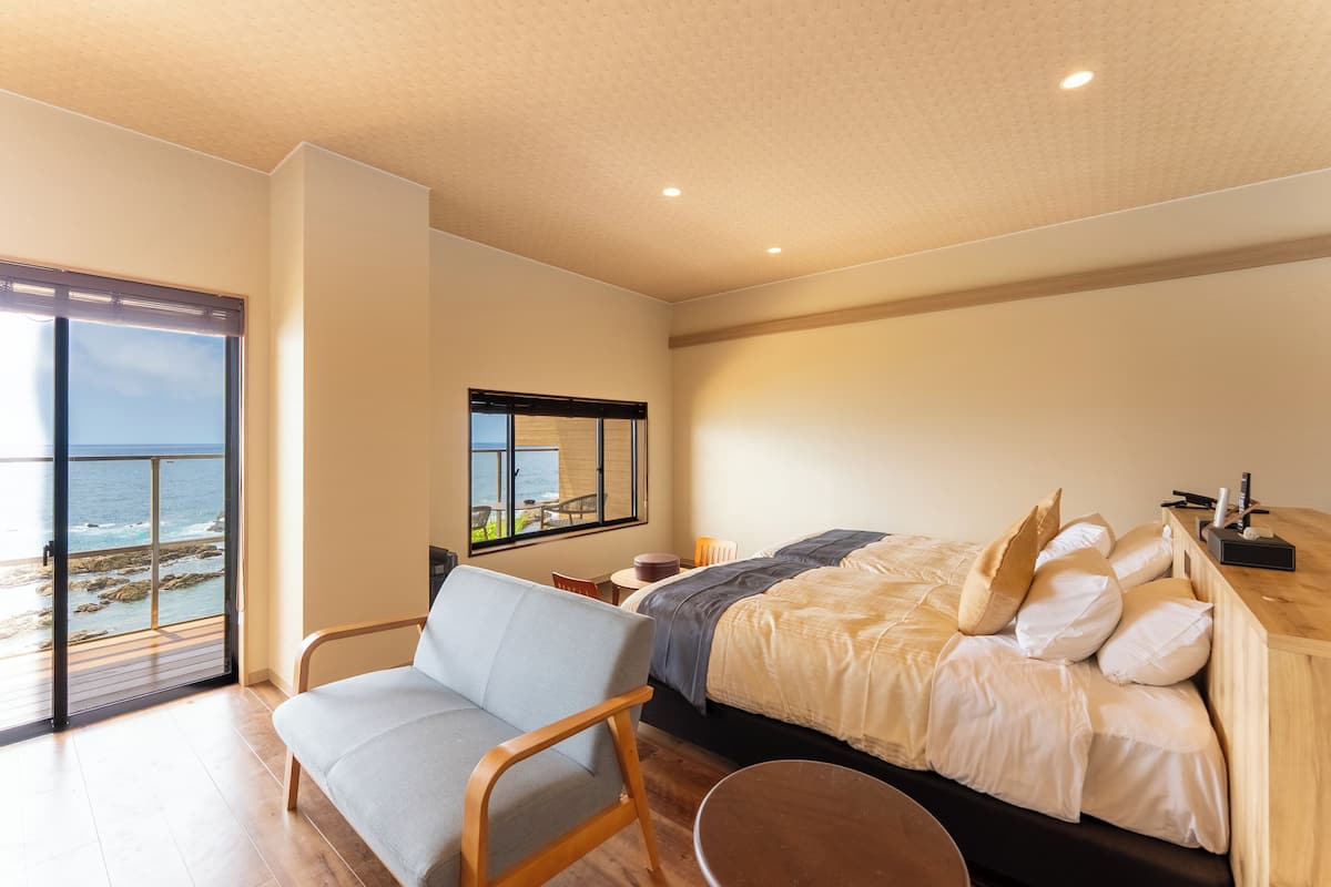 Una camera da letto con un letto, una sedia, un tavolino, una finestra vista mare e un soffitto con faretti.