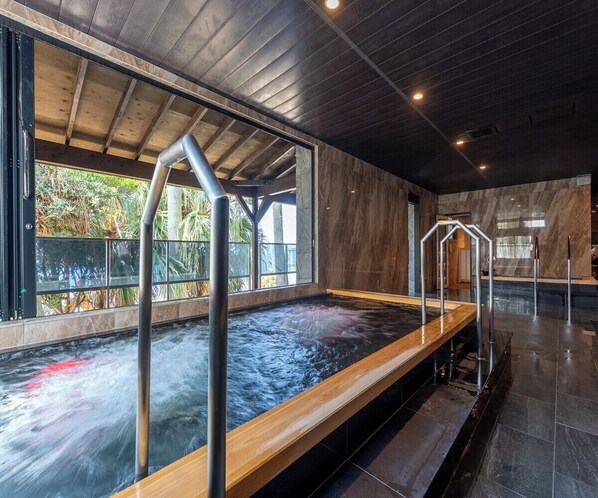 A modern indoor pool with clear glass walls, wooden deck, and metal railings.