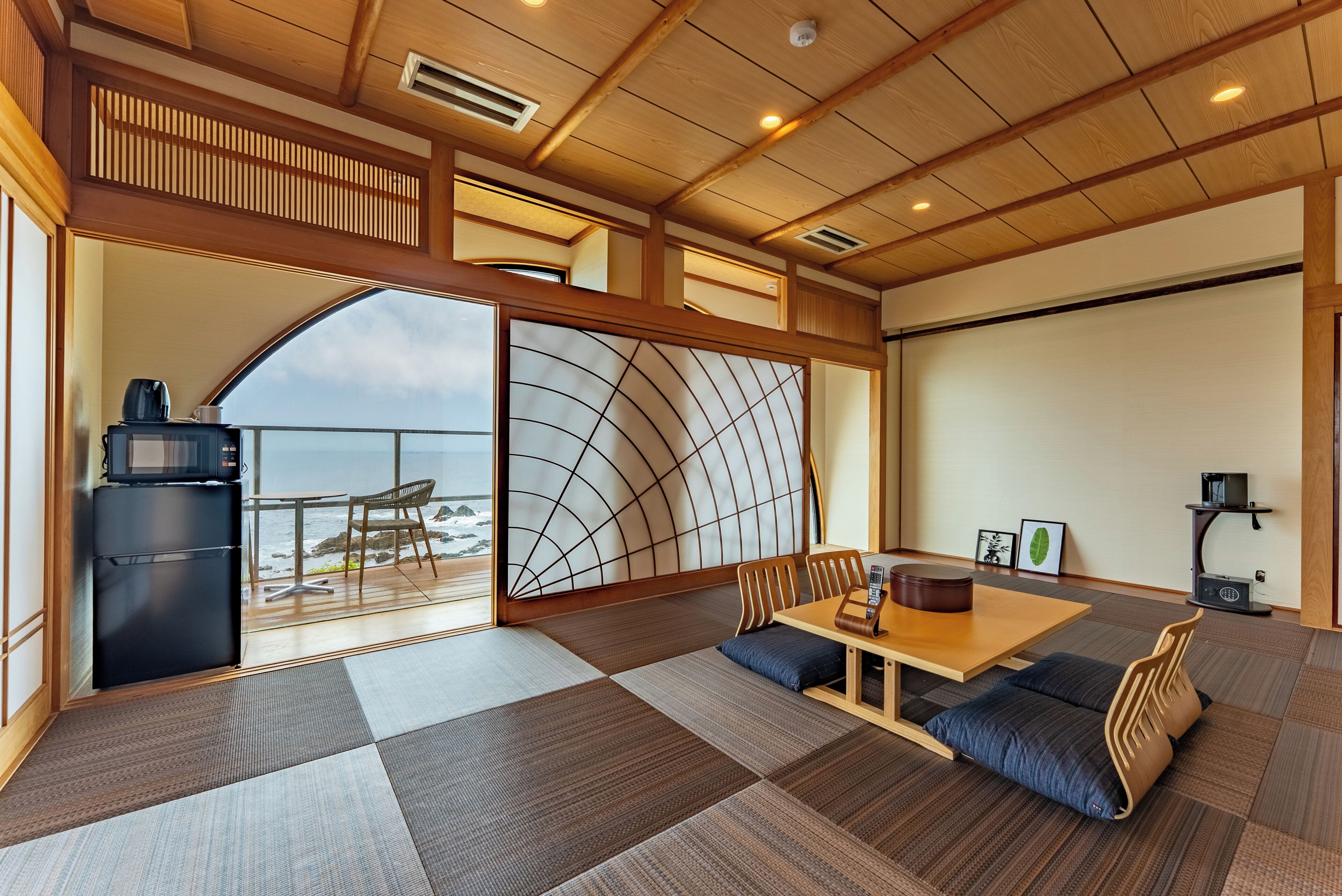 Una habitación japonesa tradicional con suelo de tatami, una mesa baja con cojines, una puerta corredera con vistas y un refrigerador negro.