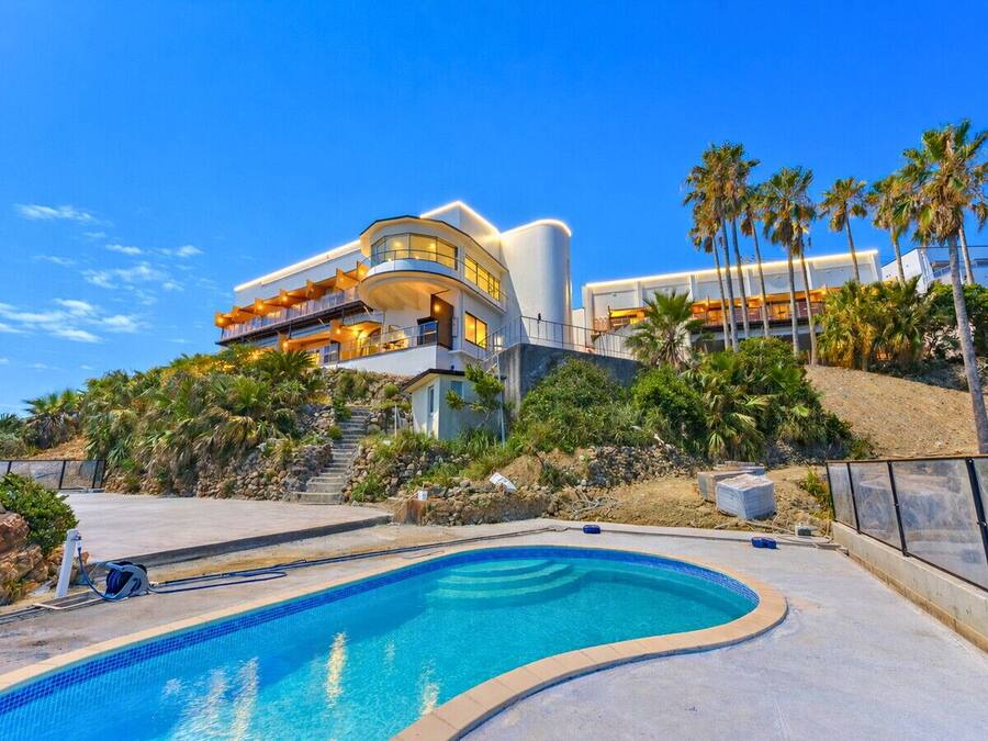 A modern house with a swimming pool, palm trees, and a clear sky.