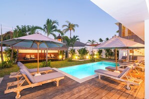 A poolside area with lounge chairs and umbrellas, surrounded by palm trees and a wooden deck. - Su Casa Boutique Hotel (Lembongan Island)