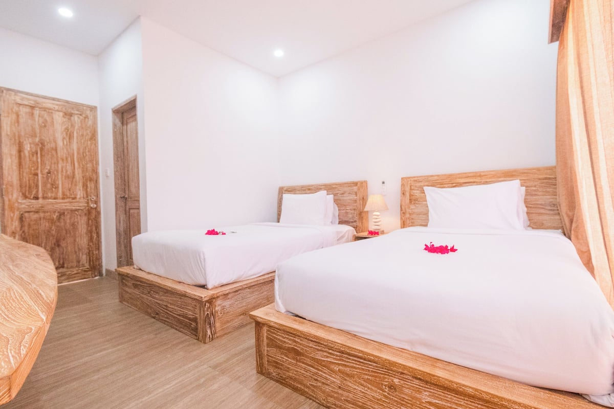 Una habitación de hotel con dos camas de madera, ropa de cama blanca y un armario de madera.