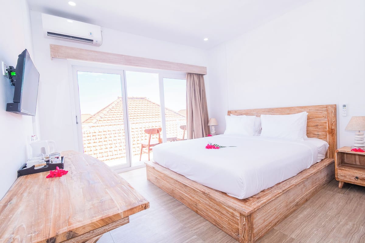 Una habitación de hotel con una cama y un escritorio de madera, un televisor y una puerta corredera de vidrio al exterior.