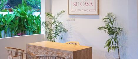 A reception desk with two chairs, a framed sign above, and potted plants on either side.