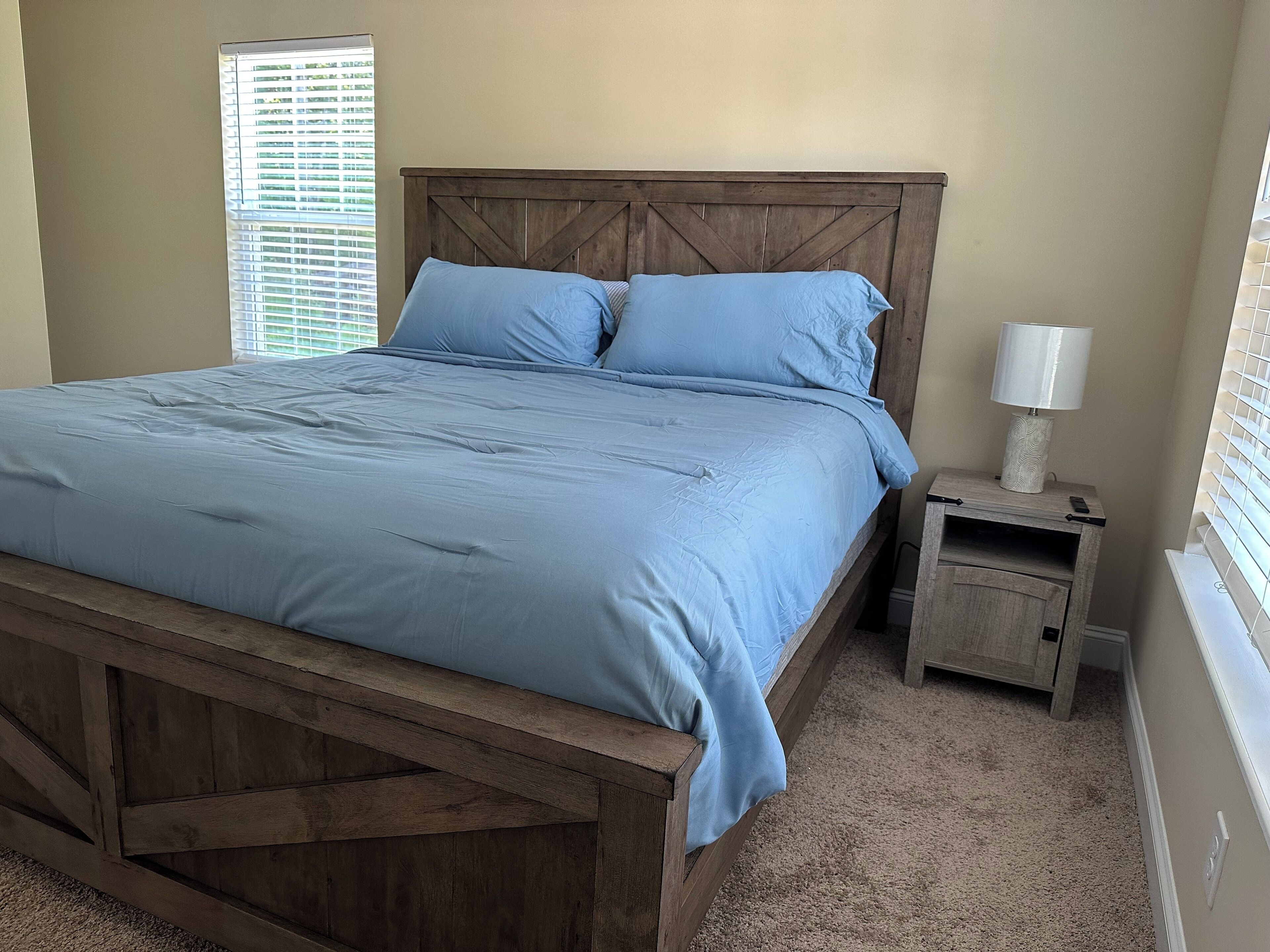 A bedroom with a wooden bed frame, a blue bedspread, and a nightstand with a lamp.