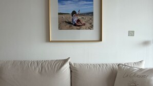 A beige sofa with a cushion that reads 'La Chaume' and a framed photograph of a person on a beach.