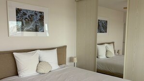 A hotel room with a bed, a large mirror, and a framed artwork on the wall.