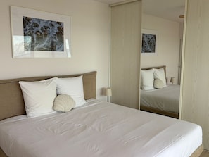 A hotel room with a bed, a large mirror, and a framed artwork on the wall.