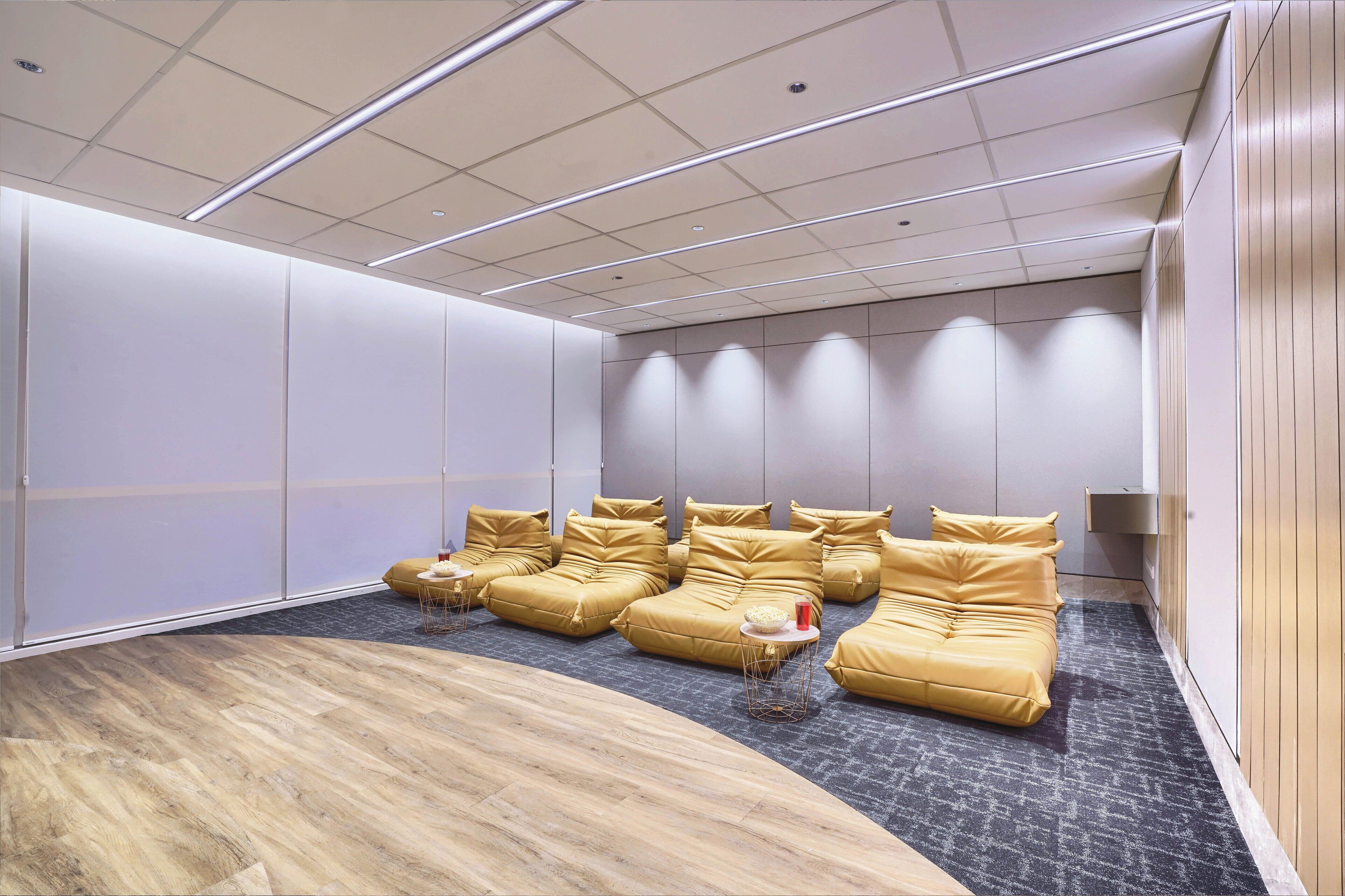 A modern lounge area with a curved wooden floor, a row of yellow sofas, and a wall-mounted TV.