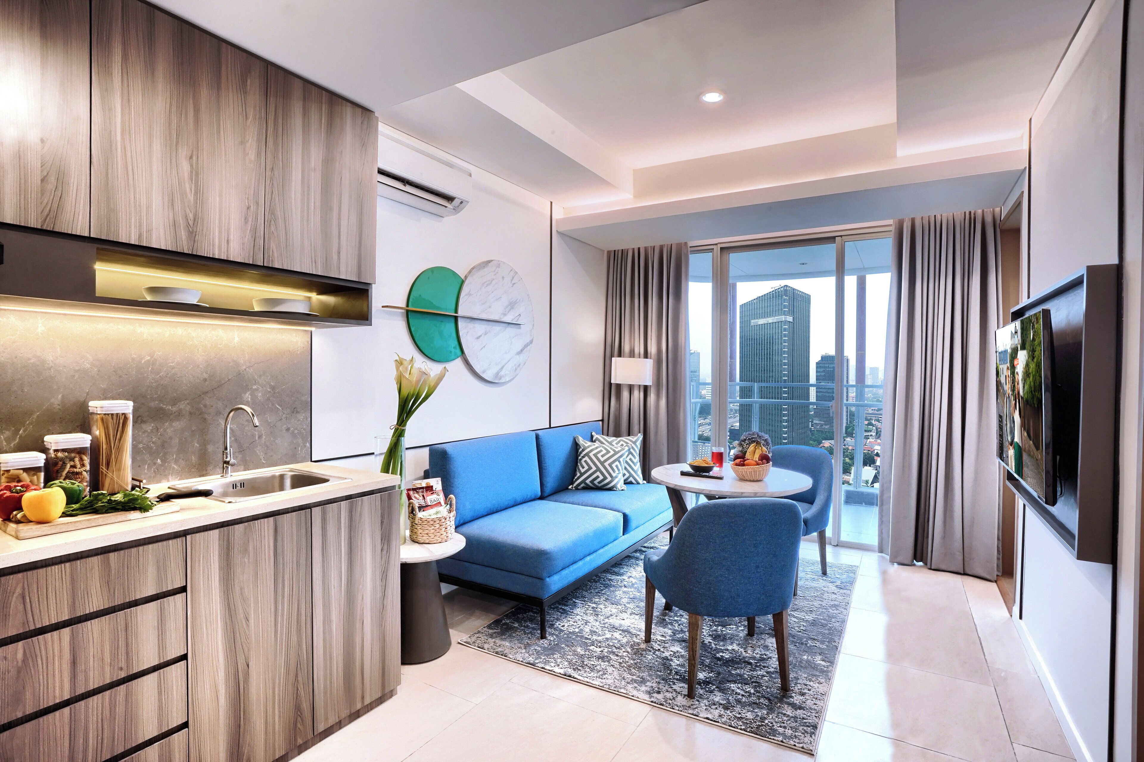 A modern apartment with a kitchen, a living area with a blue sofa, a dining table, and a large window with a city view.
