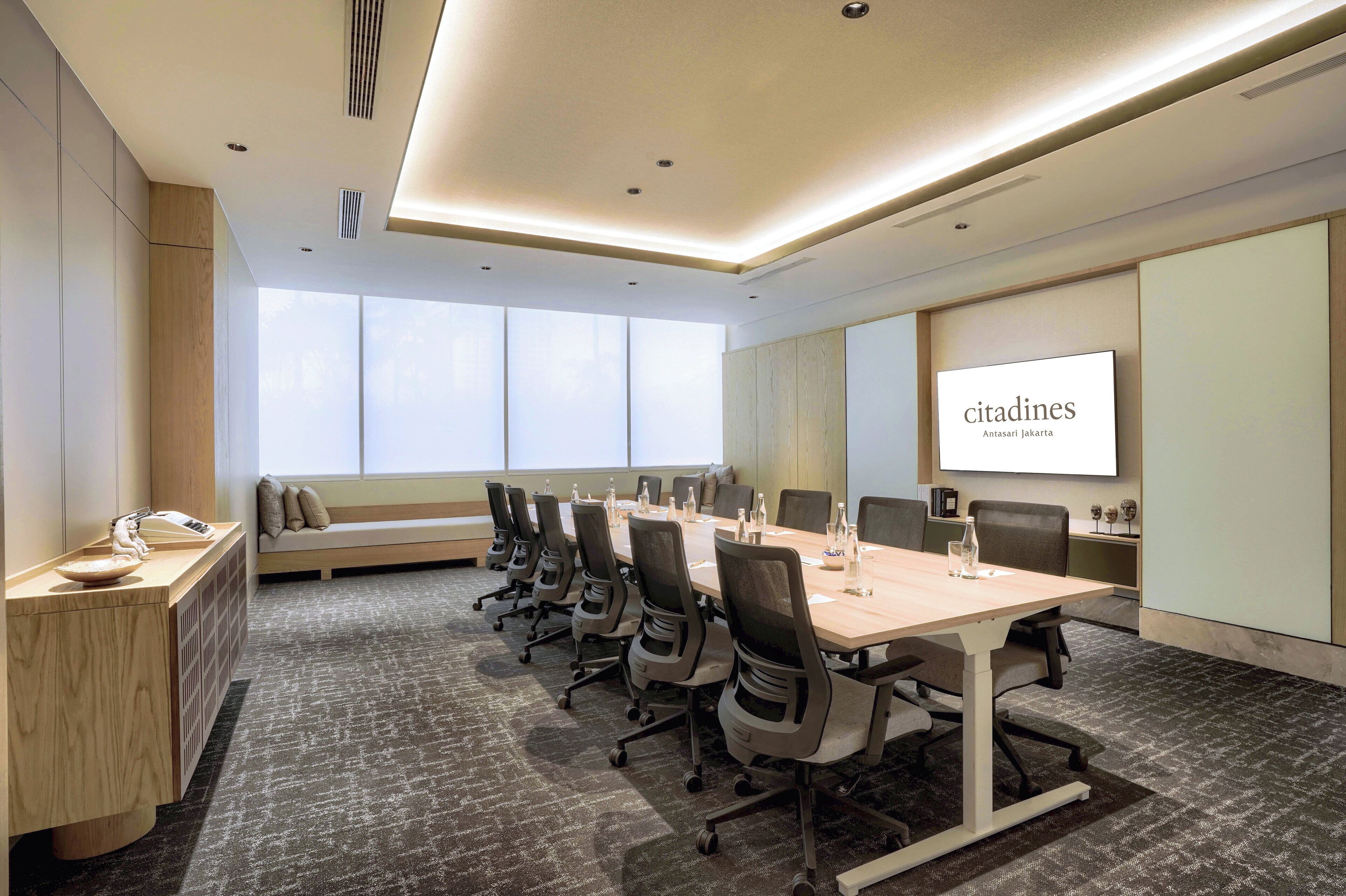 A conference room with a long table, chairs, a projector screen, and a seating area with a bench.