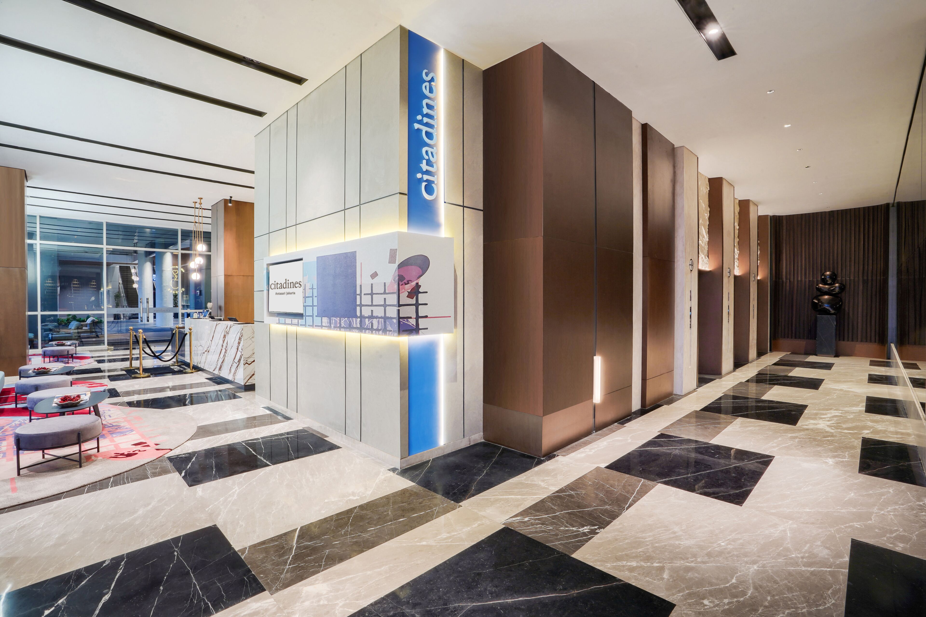 A modern lobby with a reception desk, a seating area with ottomans, and a patterned floor.