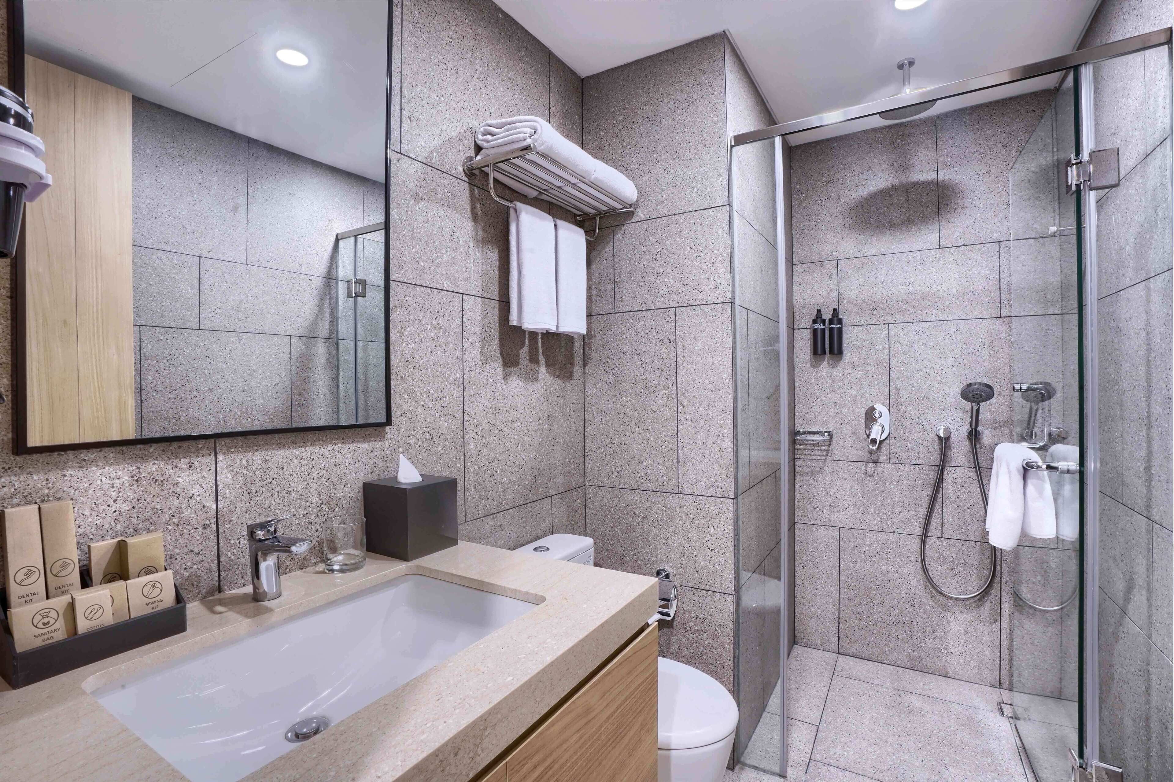 Un baño moderno con un lavamanos grande, un inodoro, una cabina de ducha de vidrio y un perchero con toallas dobladas.