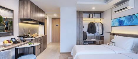 A modern hotel room with a kitchenette, a dining area, a bed, a wardrobe, and a large window.