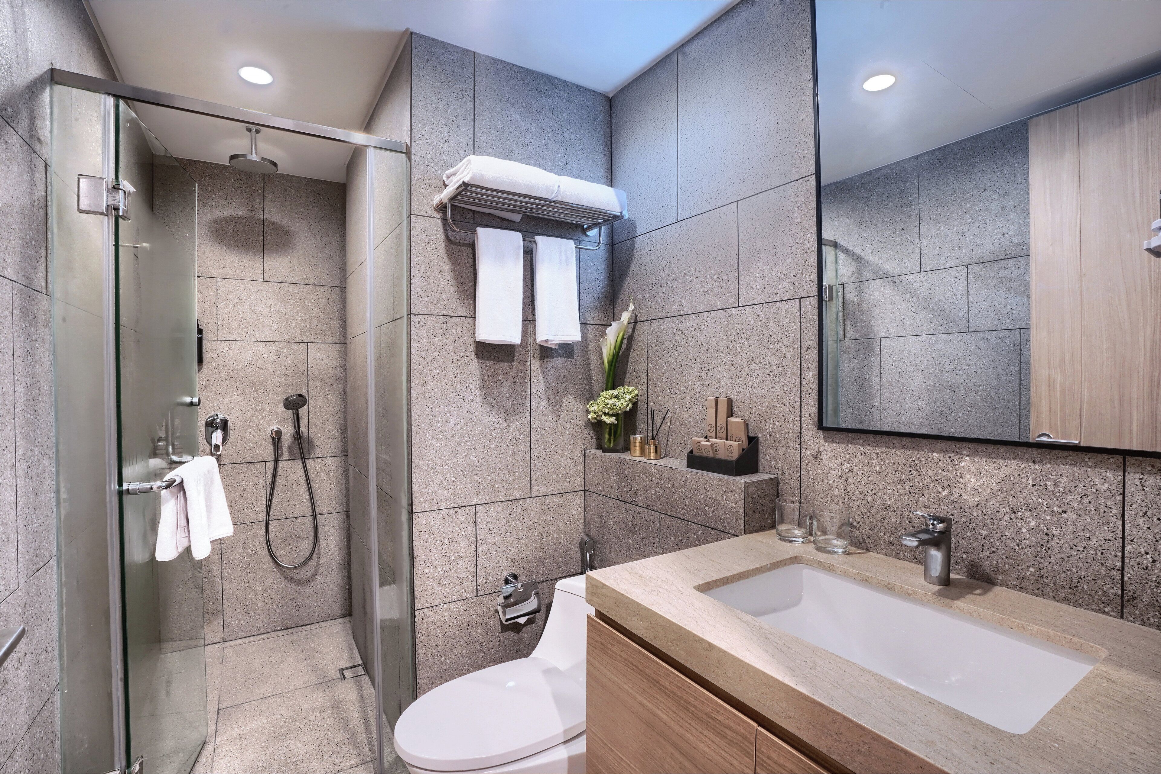 Un baño moderno con ducha envuelta en vidrio, inodoro blanco y lavamanos color beige con espejo superior.