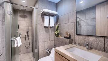 Un baño moderno con ducha envuelta en vidrio, inodoro blanco y lavamanos color beige con espejo superior.