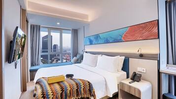 A hotel room with a large bed, a bedside table with a phone, a window with a city view, and a wall-mounted TV.
