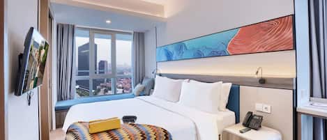 A hotel room with a large bed, a bedside table with a phone, a window with a city view, and a wall-mounted TV.